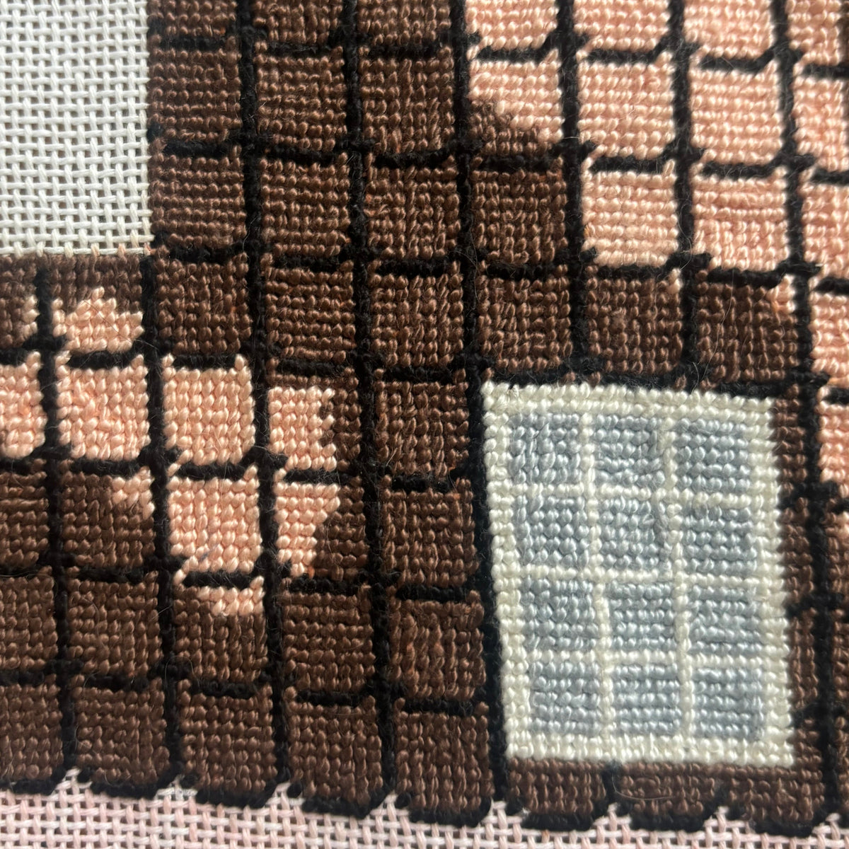 An image showing the roof of a house on a needlepoint canvas. This section of the canvas is completed