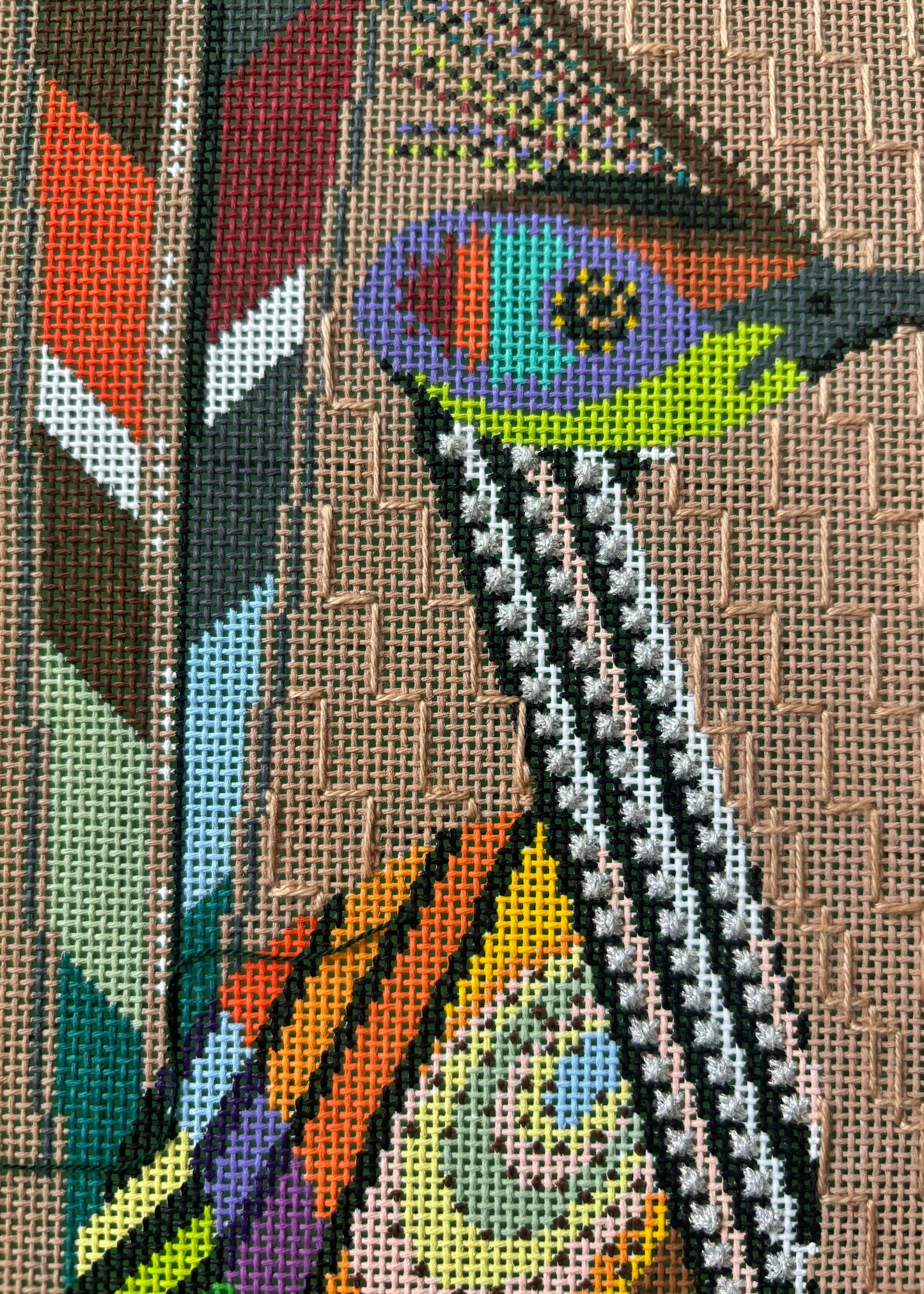 an image of a needlepoint canvas focusing on the face of the bird shown in the image.
