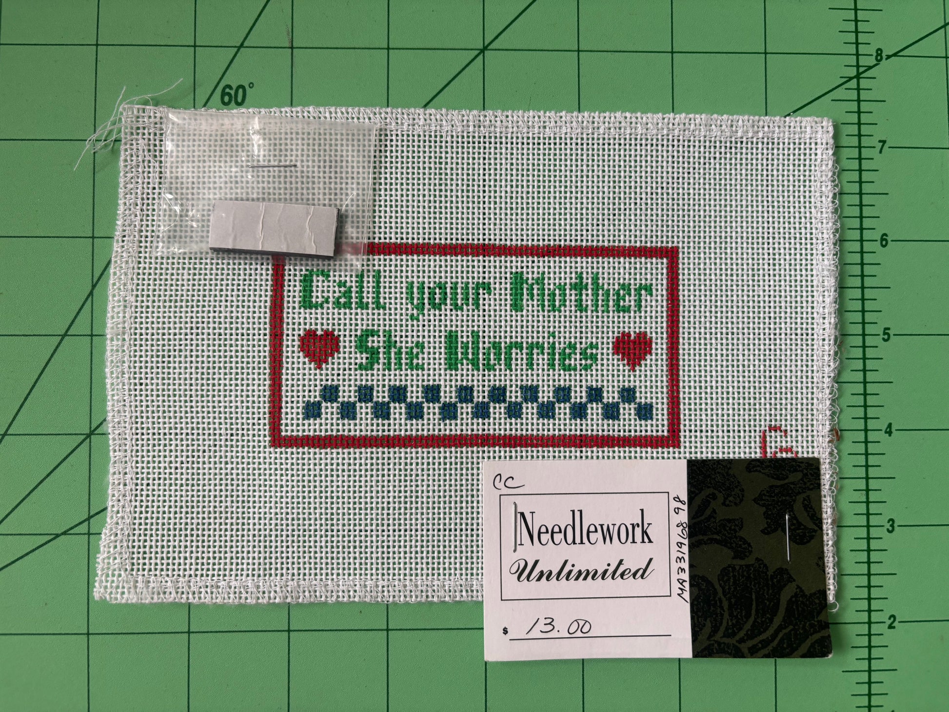 A needlepoint canvas that says "Call your mother, she worries" with hearts and a checkered border