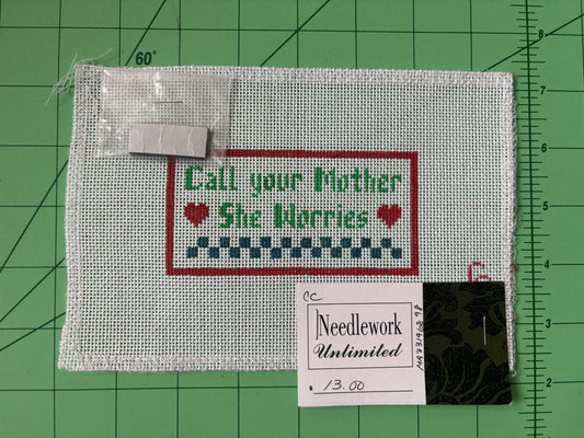 A needlepoint canvas that says "Call your mother, she worries" with hearts and a checkered border