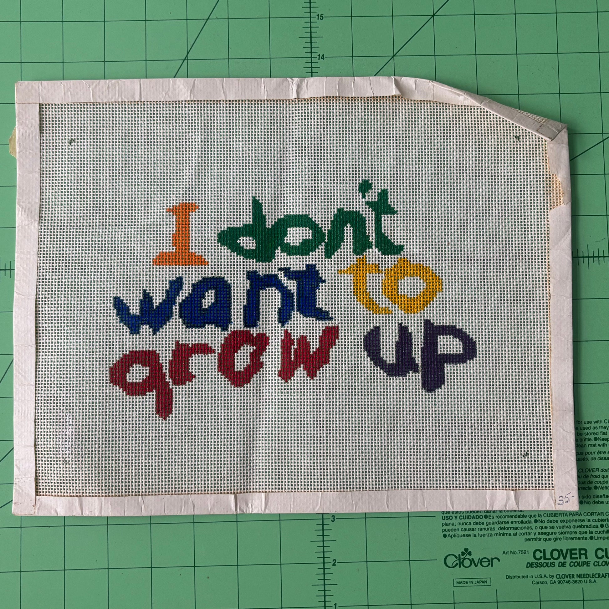 An image of a needlepoint canvas that says "I don't want to grow up" in multi-colored text as if a child wrote it. 