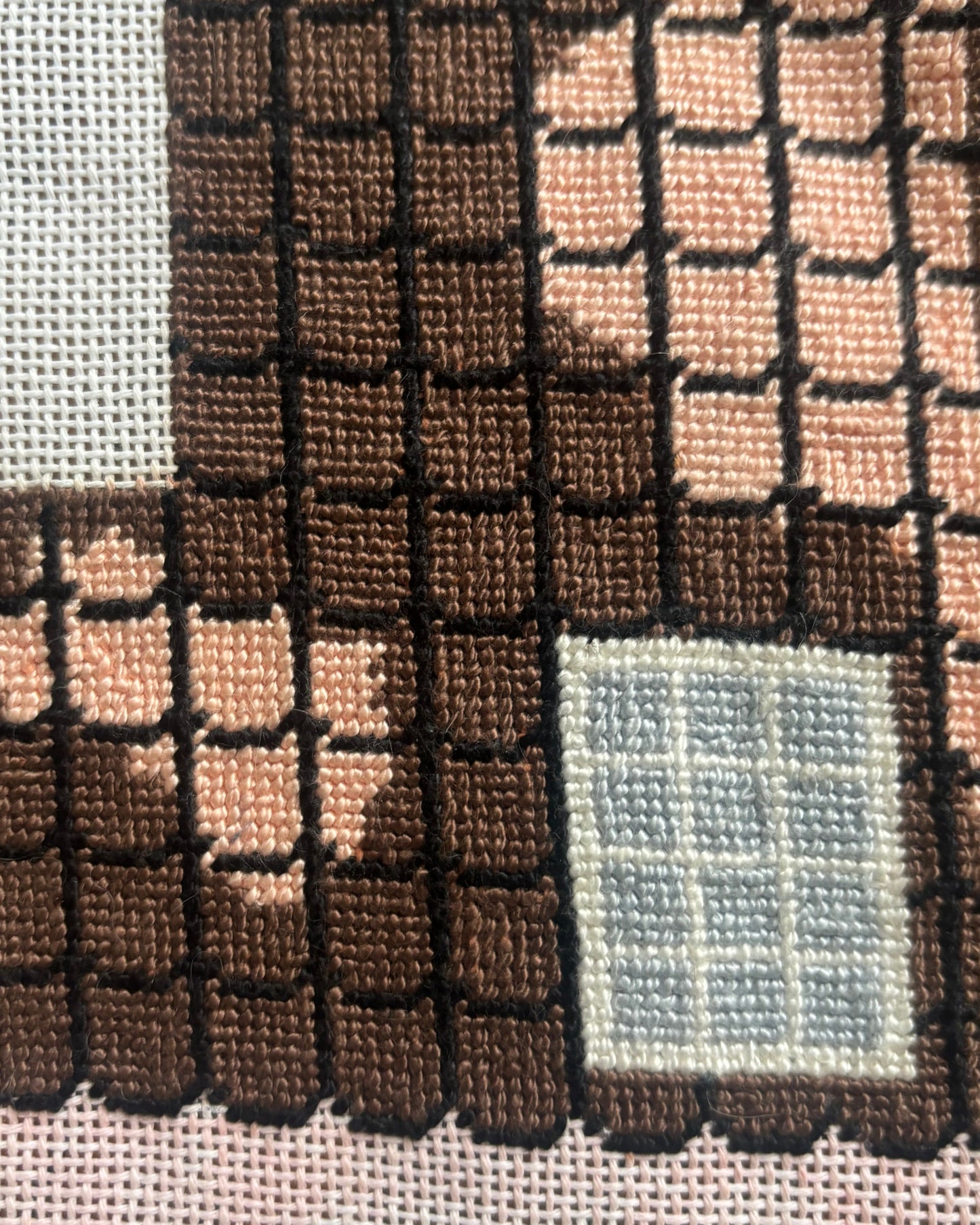 An image showing the roof of a house on a needlepoint canvas. This section of the canvas is completed 